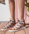 A woman wearing Bed Stu Shirin II lace-up sandals on a wooden deck.