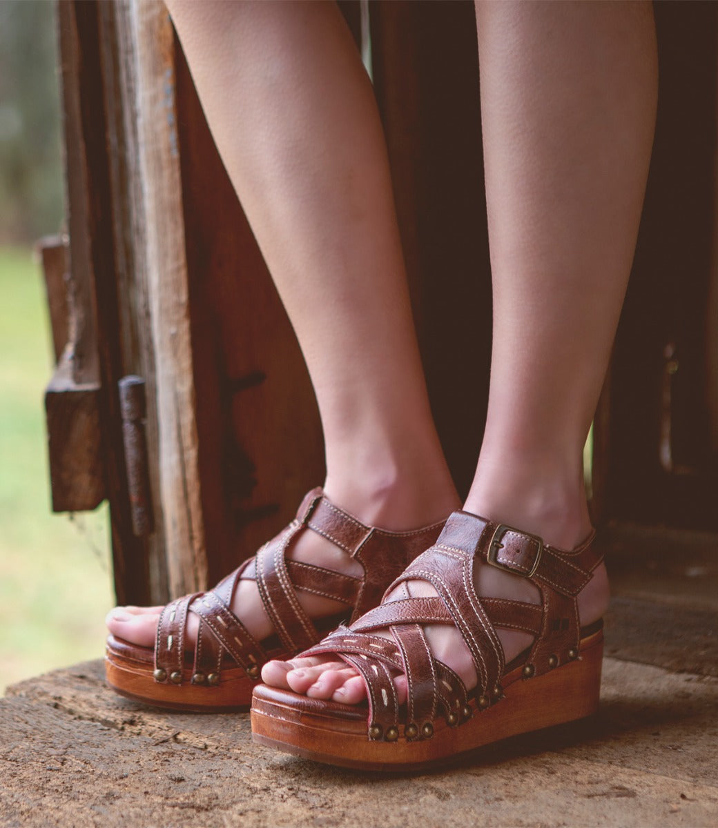 A woman wearing a pair of Bed Stu Shirley sandals on a wooden floor.