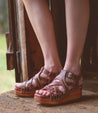 A woman wearing a pair of Bed Stu Shirley sandals on a wooden floor.
