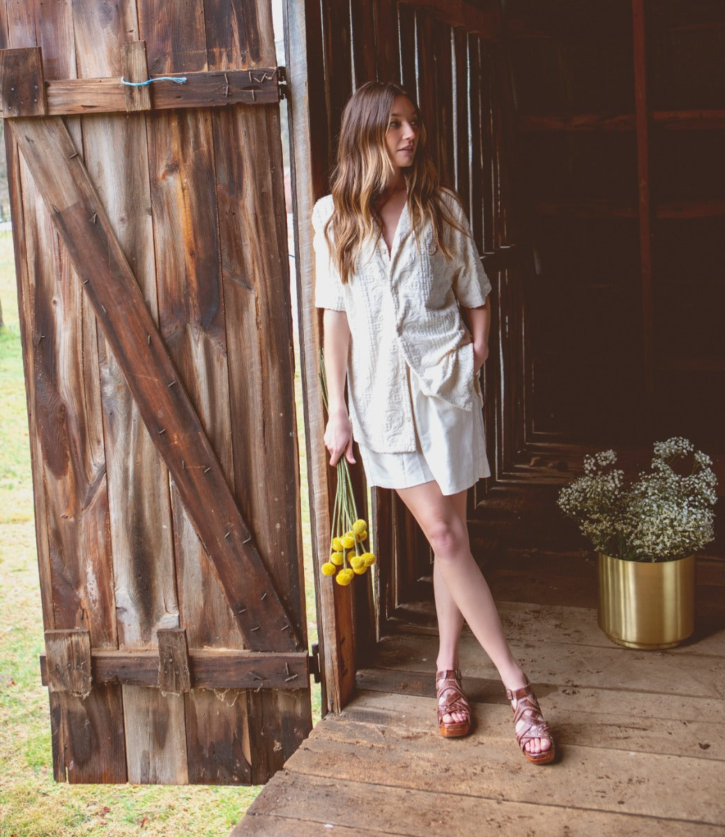 A woman wearing a white Shirley dress and Bed Stu sandals standing in front of a barn.