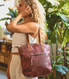 A woman holding a Bed Stu Skye II burgundy leather tote bag.