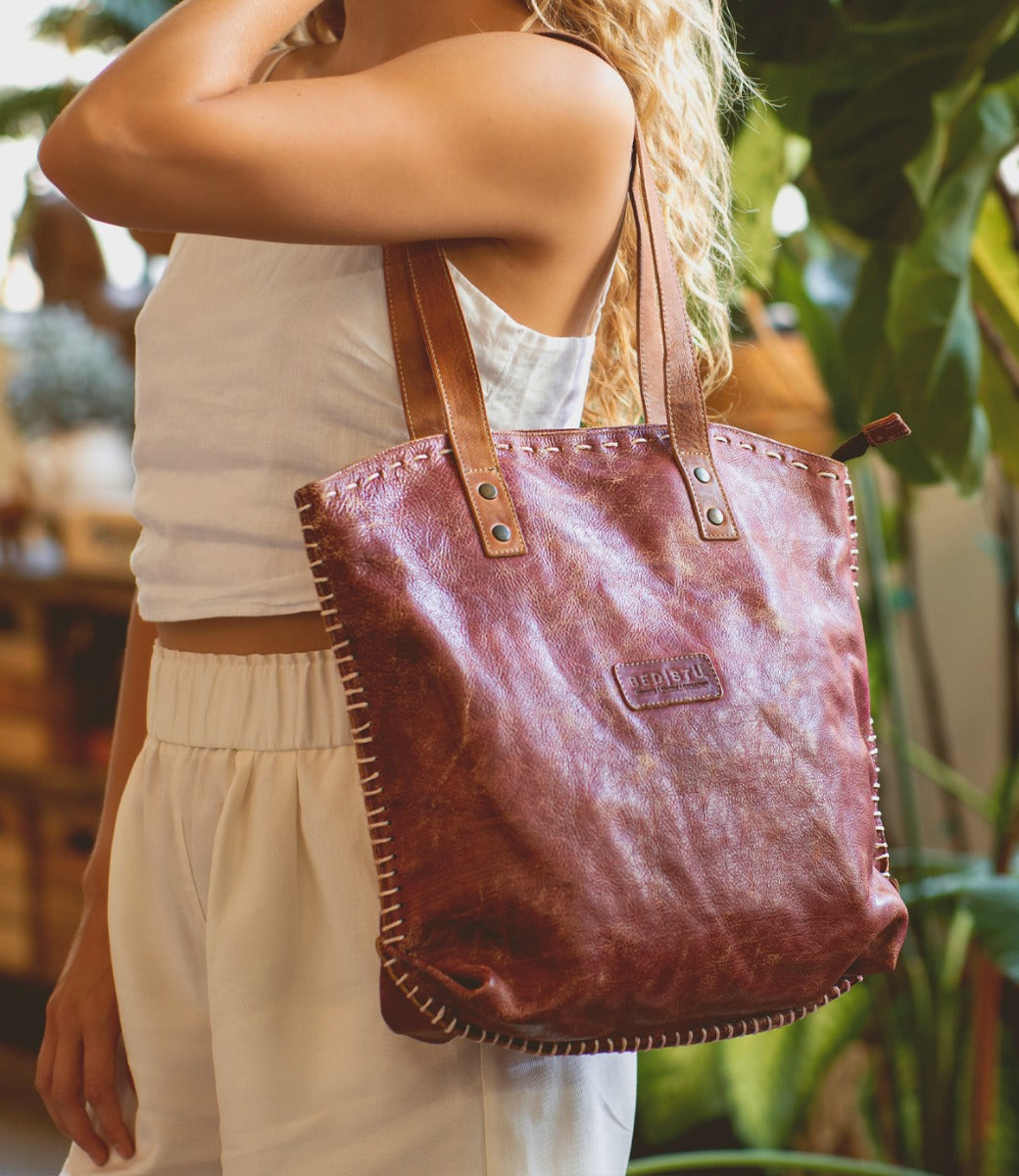 A woman holding a Skye II leather tote bag by Bed Stu.