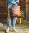 A woman holding a Skye II Bed Stu leather tote bag.