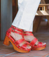 A woman wearing Bed Stu red Sloane sandals and white pants.