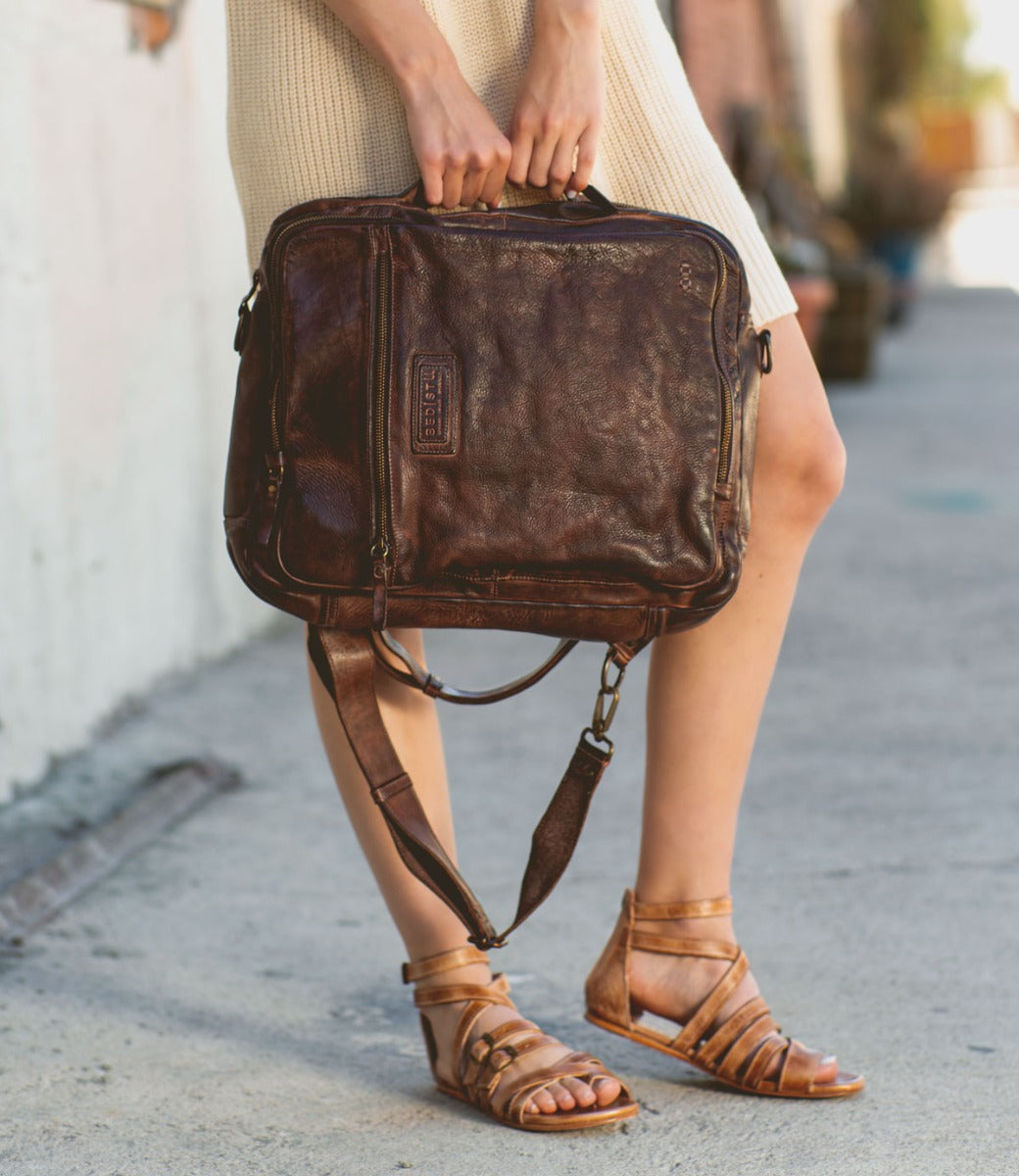 A woman holding a brown leather Bed Stu Socrates briefcase.