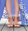 A woman's feet in Bed Stu tan sandals on a wooden deck.