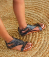 A woman wearing a pair of black Soto sandals by Bed Stu on a straw rug.