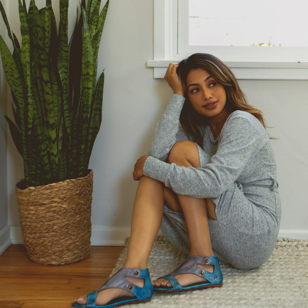 A woman sitting on the floor wearing Bed Stu leather sandals.