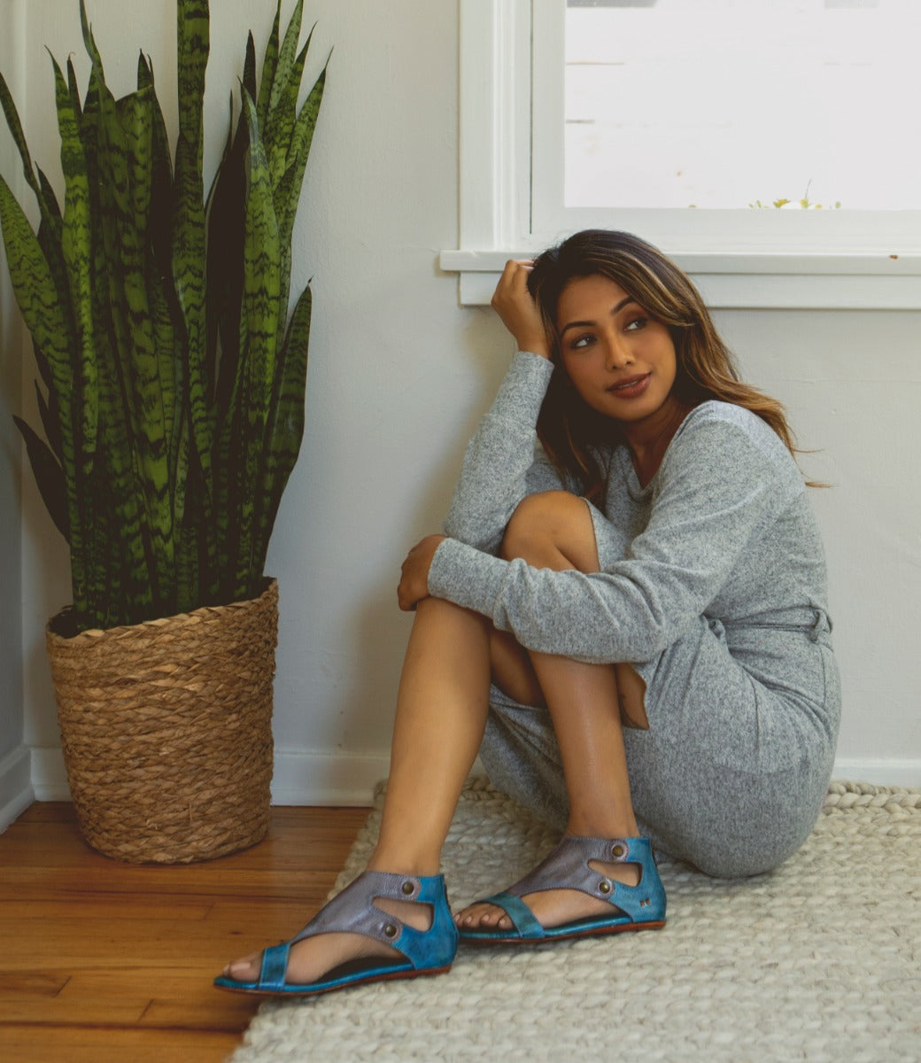 A woman sitting on the floor wearing Bed Stu leather sandals.