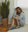 A woman sitting on the floor wearing Bed Stu leather sandals.