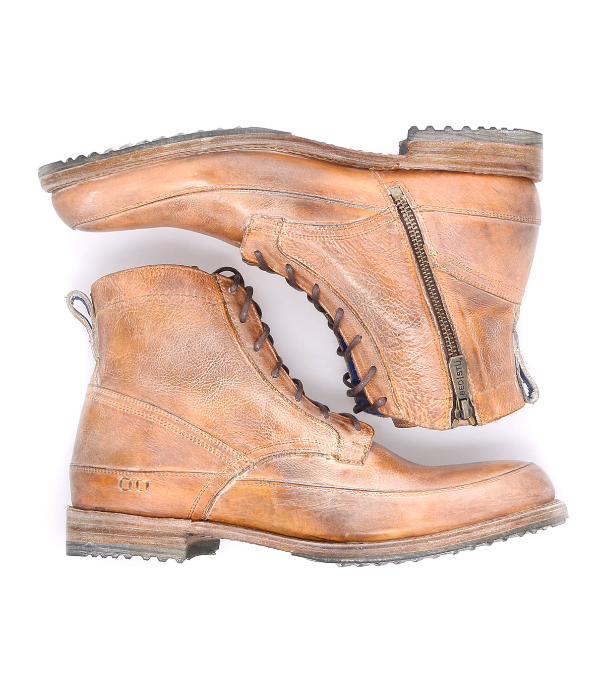 A pair of worn brown leather lace-up ankle boots with side zippers and well-treaded soles, arranged in a crossover layout on a white background by Bed Stu's Spiker boots.