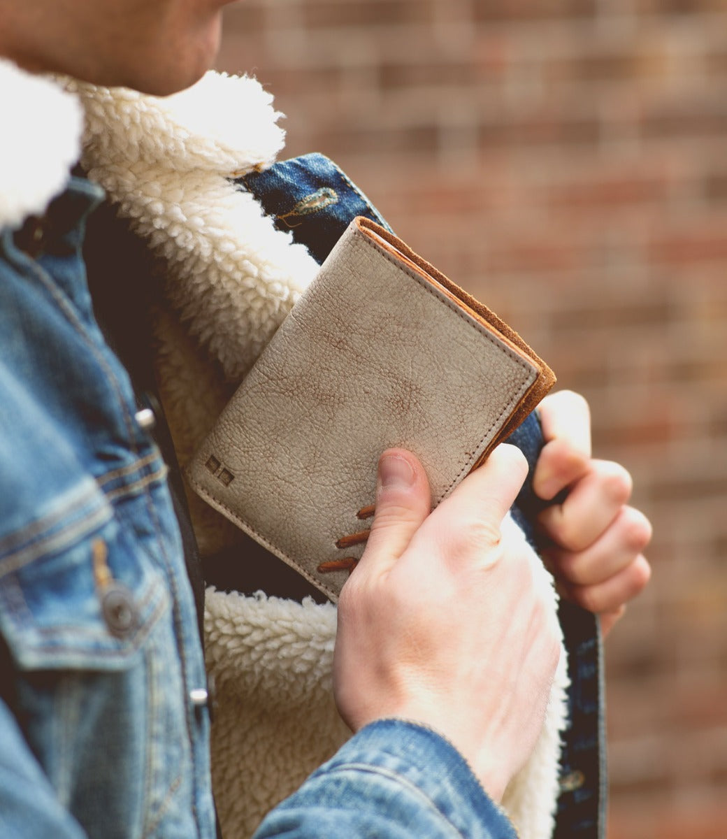 A man is holding a Stardust wallet in front of a brick wall, made by Bed Stu.