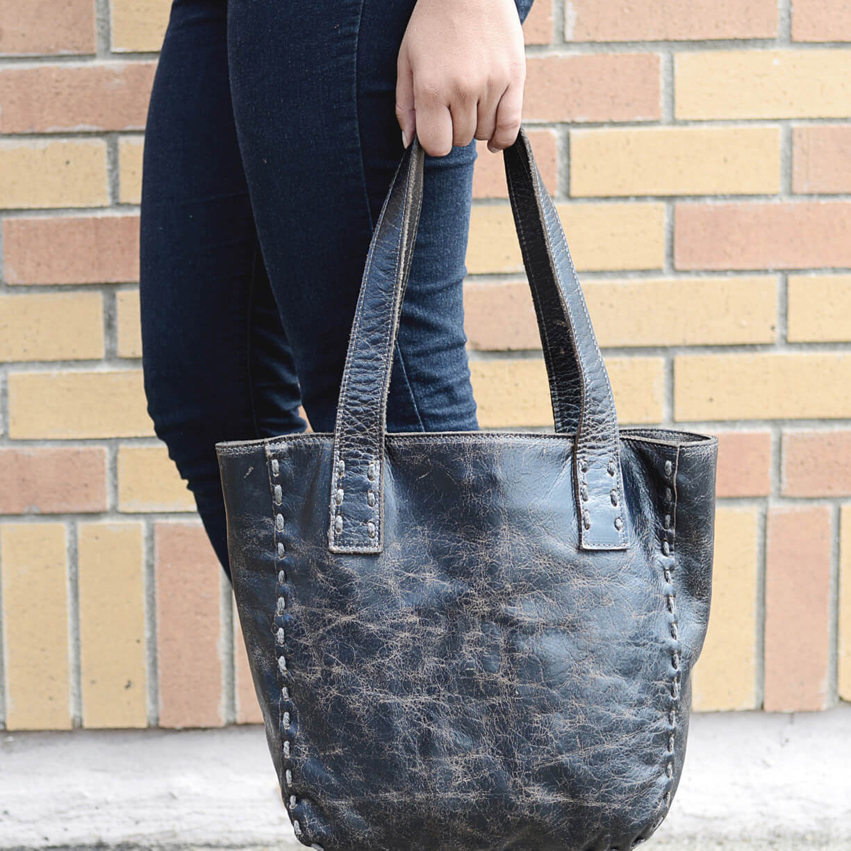 A woman holding a black leather Bed Stu Stevie tote bag.