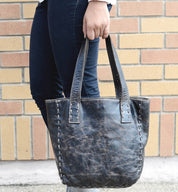A woman holding a black leather Bed Stu Stevie tote bag.