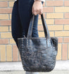 A woman holding a black leather Bed Stu Stevie tote bag.