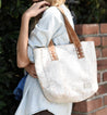 A woman holding a white Bed Stu Stevie tote bag in front of a brick wall.