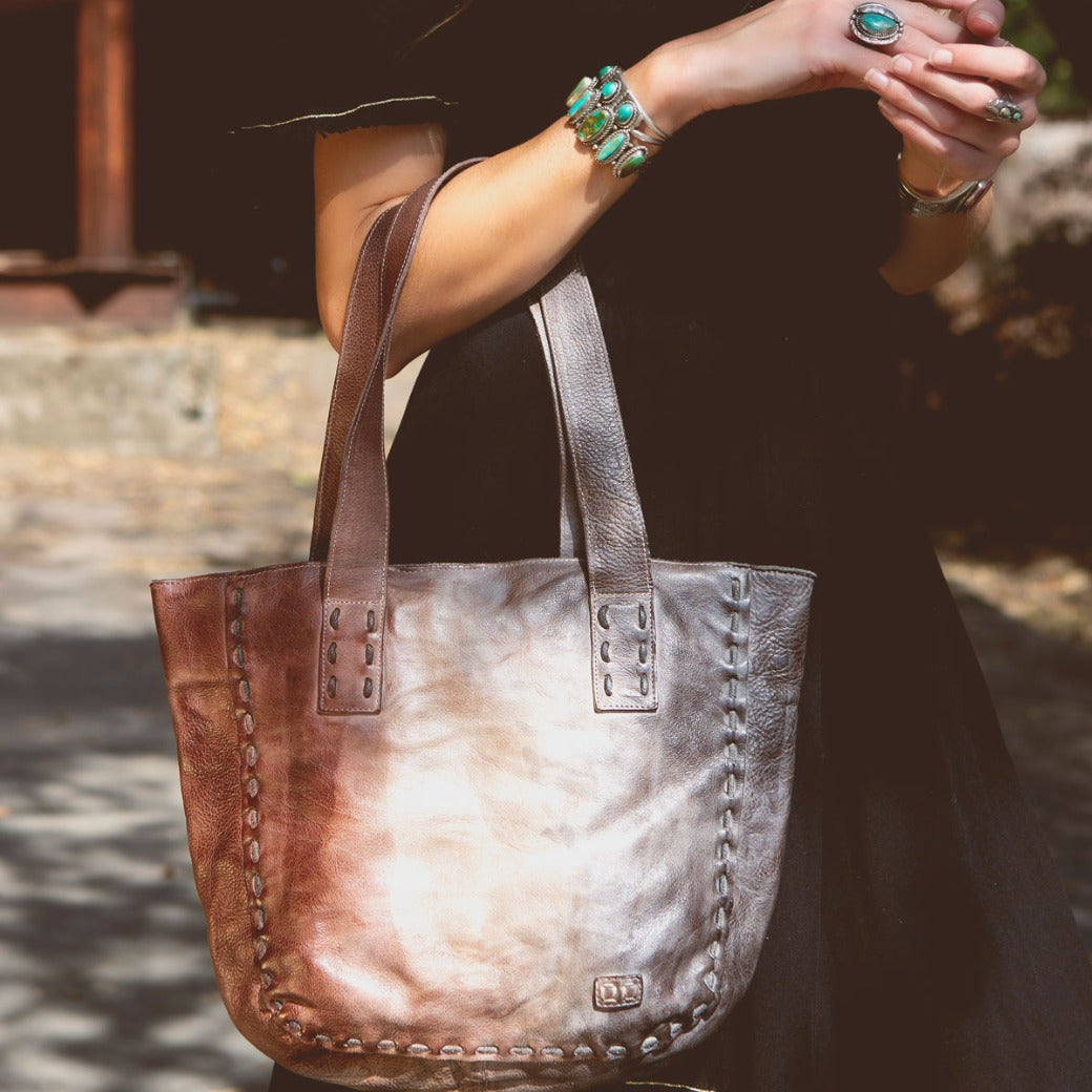 A woman is holding a brown leather Bed Stu Stevie tote bag.