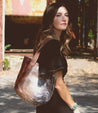 A woman wearing a black dress holding a brown Bed Stu Stevie tote bag.