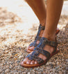 A woman wearing a pair of Bed Stu Sue sandals on gravel.