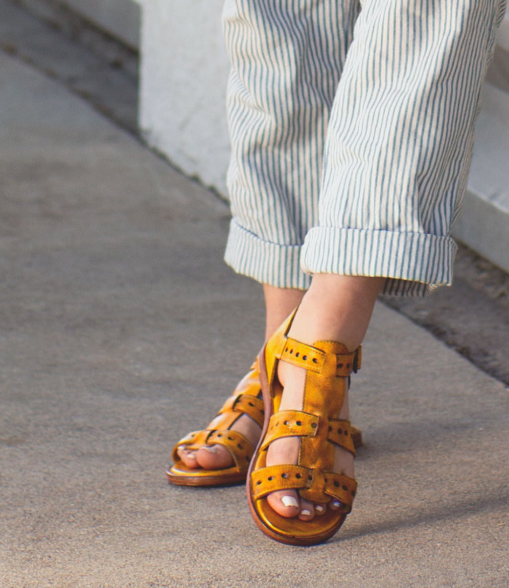 A woman wearing striped pants and yellow Bed Stu sandals.