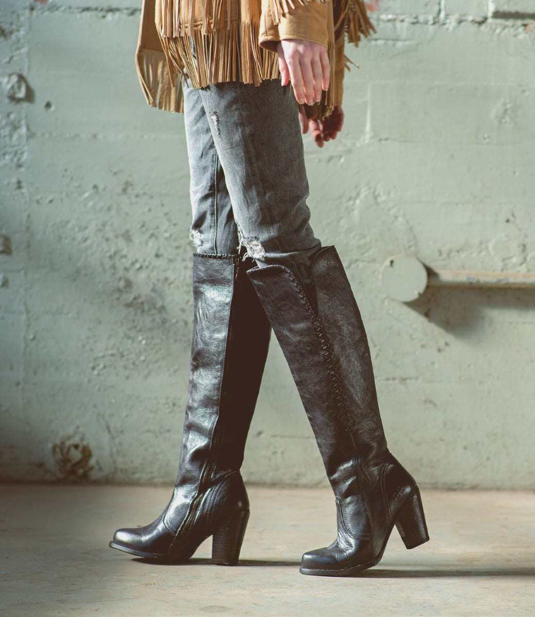 A woman wearing black Sumaya boots and a Bed Stu fringe jacket.