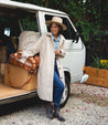 A woman wearing a Tabitha hat and coat standing next to a Bed Stu vw van.