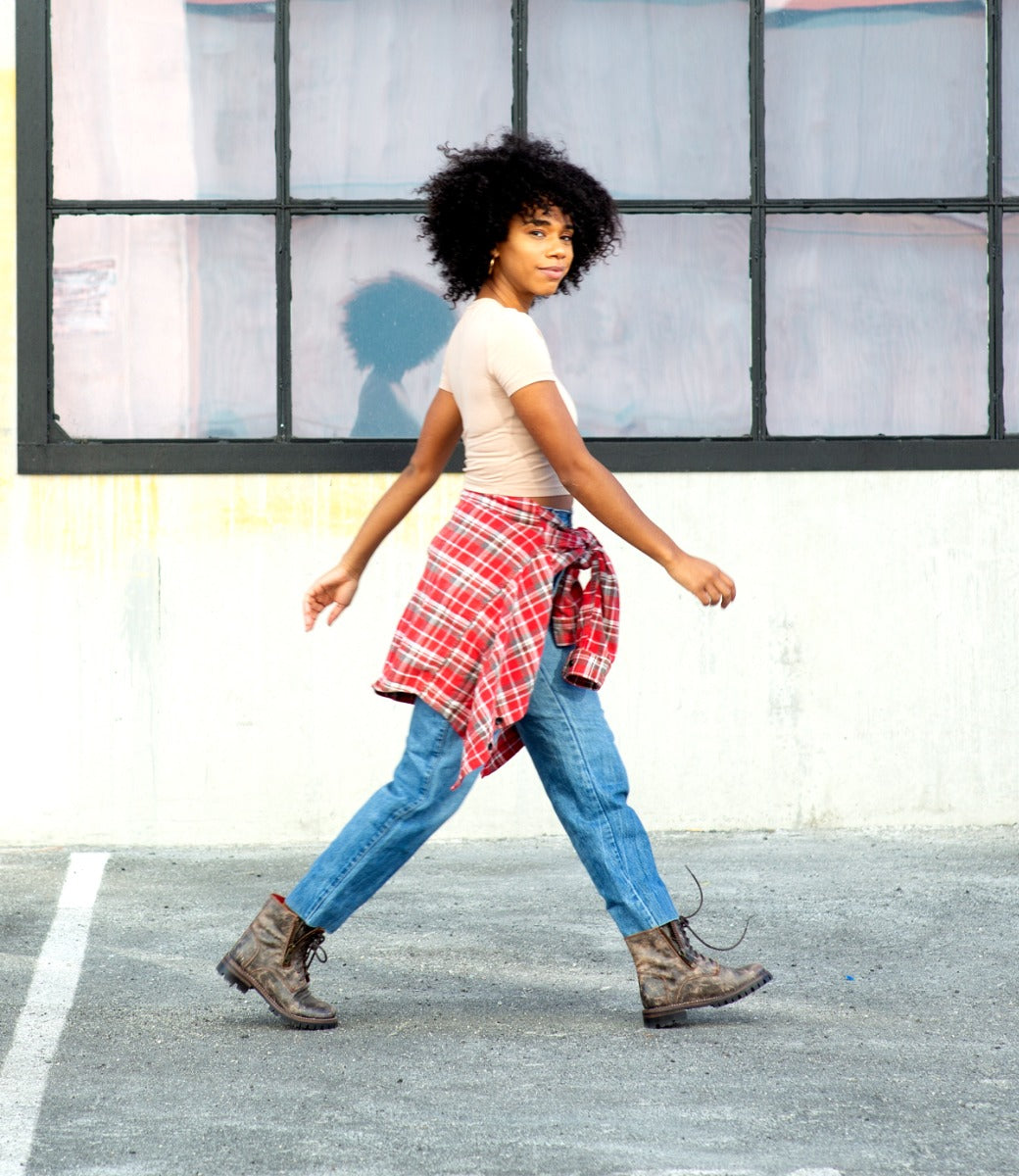 A woman walking in a parking lot wearing Bed Stu's Tactic Trek plaid shirt and jeans.