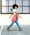 A woman walking in a parking lot wearing Bed Stu's Tactic Trek plaid shirt and jeans.