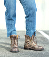A person in Tactic Trek jeans and Bed Stu boots standing in a parking lot.