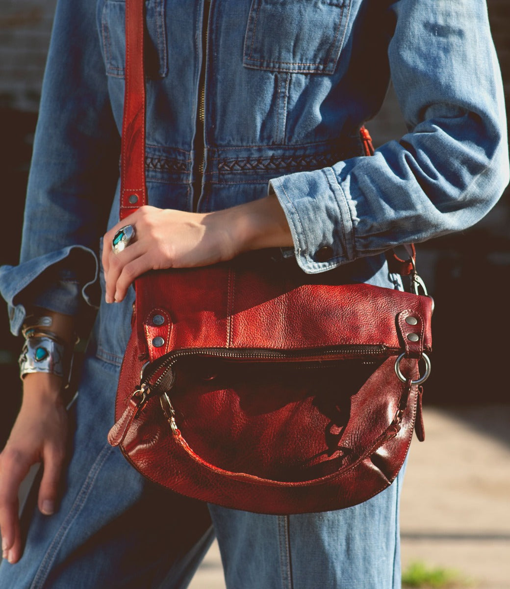 A woman in denim overalls holding a Bed Stu Tahiti red leather purse.