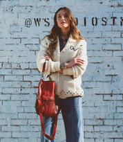 A woman is standing in front of a brick wall holding a Bed Stu Tahiti bag.