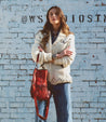 A woman is standing in front of a brick wall holding a Bed Stu Tahiti bag.