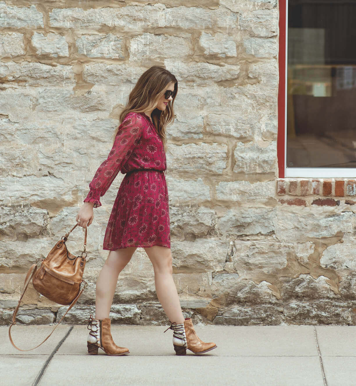A woman walking down the street in a pink dress and Bed Stu Tahiti boots.
