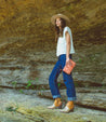 A woman wearing Tania jeans and a Bed Stu hat standing on a rock.