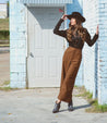 A woman leaning against a wall wearing a Tania hat and wide leg pants by Bed Stu.