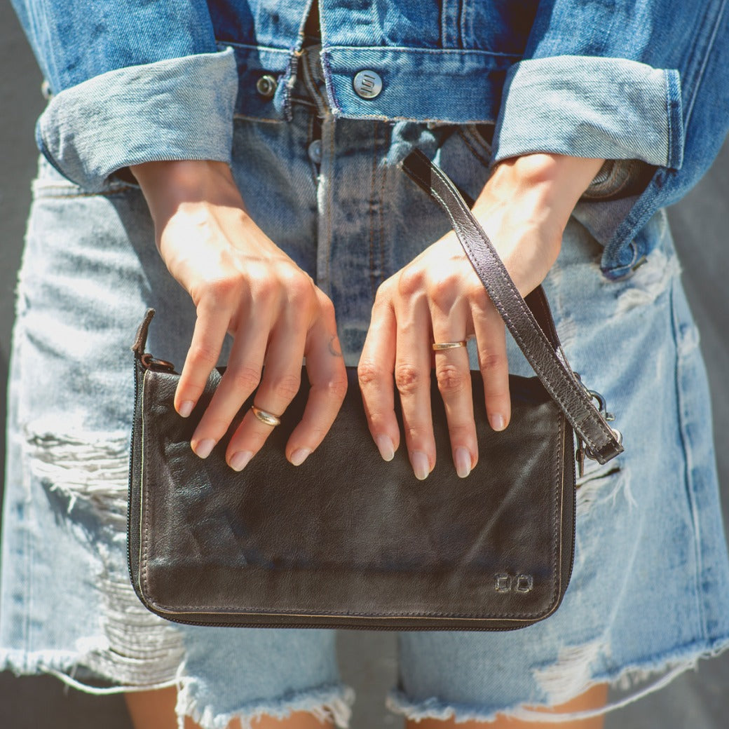 A woman holding a Bed Stu Templeton II black leather clutch.