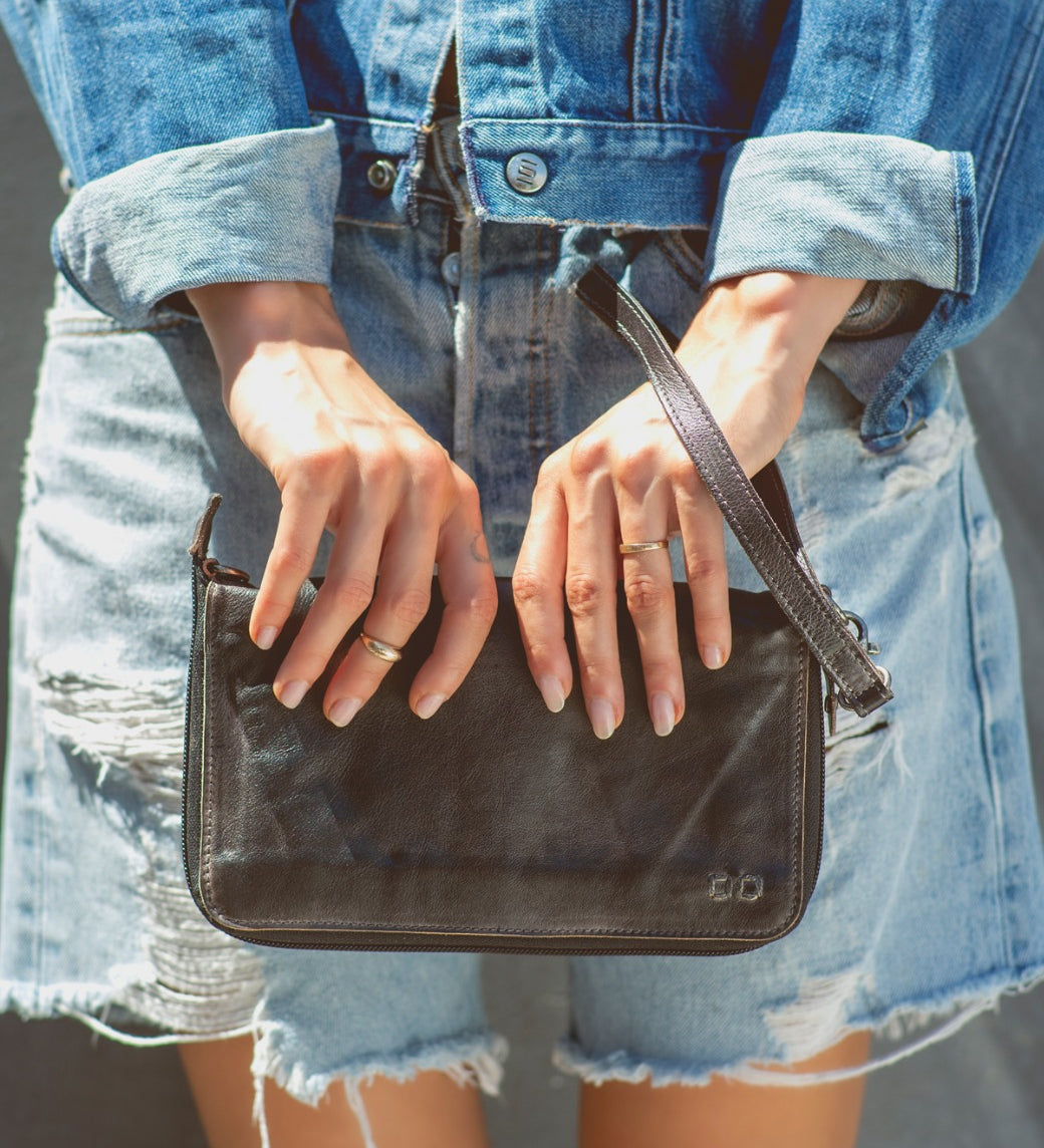 A woman holding a Bed Stu Templeton II black leather clutch.