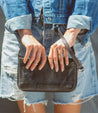 A woman holding a Bed Stu Templeton II black leather clutch.