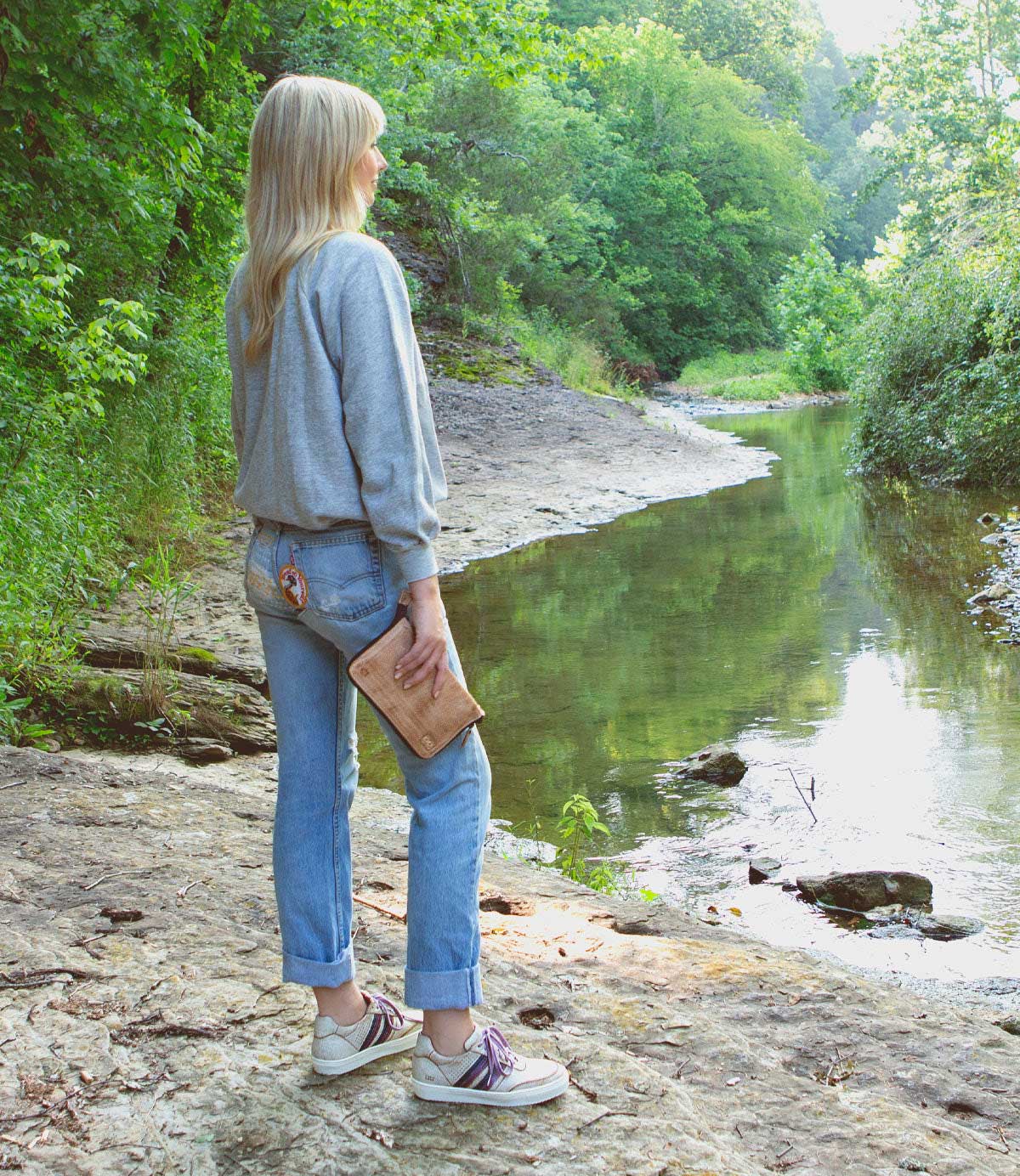 A woman holding a Bed Stu Templeton II oat colored leather clutch.