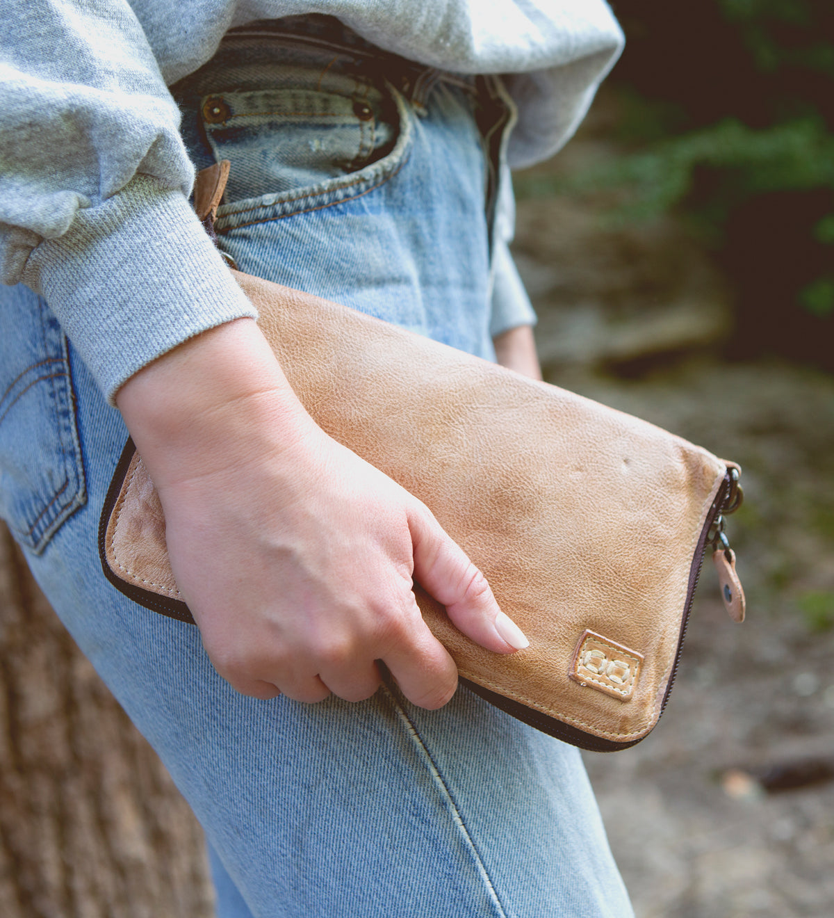 A woman holding a Bed Stu Templeton II oat colored clutch.