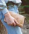 A woman holding a Bed Stu Templeton II oat colored clutch.