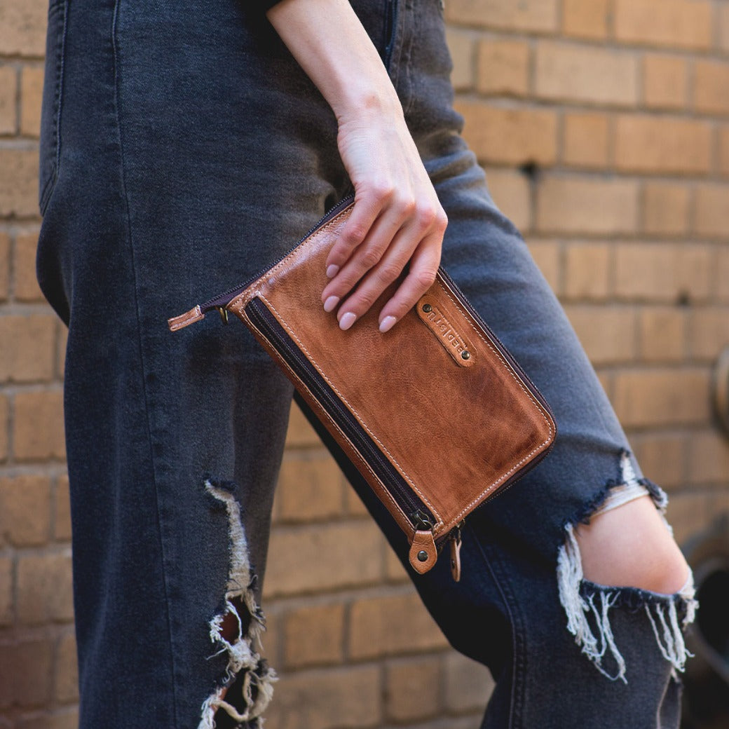 A woman holding a Bed Stu Templeton II tan leather clutch.