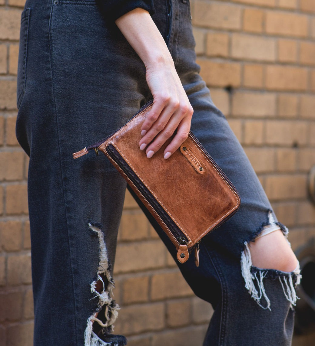 A woman holding a Bed Stu Templeton II tan leather clutch.