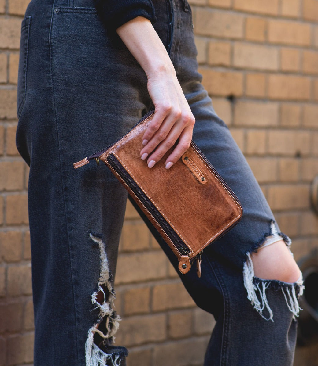 A woman holding a Bed Stu Templeton II tan leather clutch.