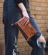 A woman holding a Bed Stu Templeton II tan leather clutch.