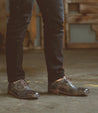 A man wearing a pair of Bed Stu Thorn shoes standing in a warehouse.