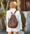 A woman wearing a brown leather Bed Stu Tommie backpack walking down the street.