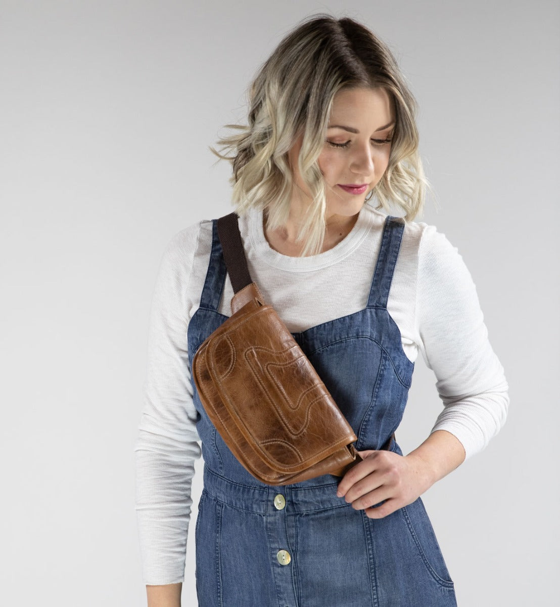 A woman wearing Travers denim overalls and a Bed Stu brown fanny bag.