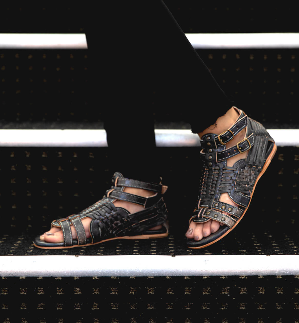 A person wearing a pair of black Bed Stu Claire sandals on stairs.