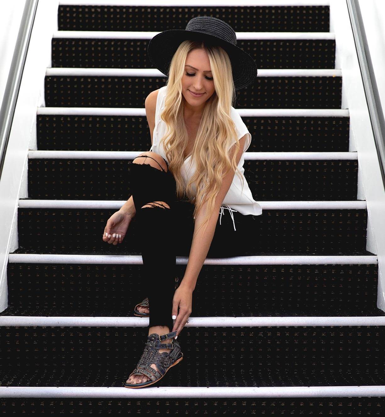 A blonde woman sitting on the stairs in a Claire by Bed Stu hat.